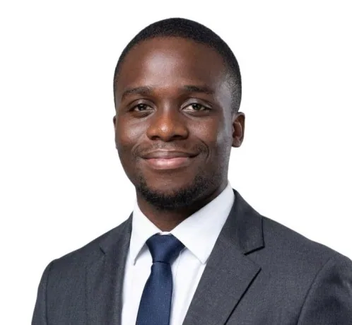 Portrait of David Oyelade in a grey suit and navy tie, smiling